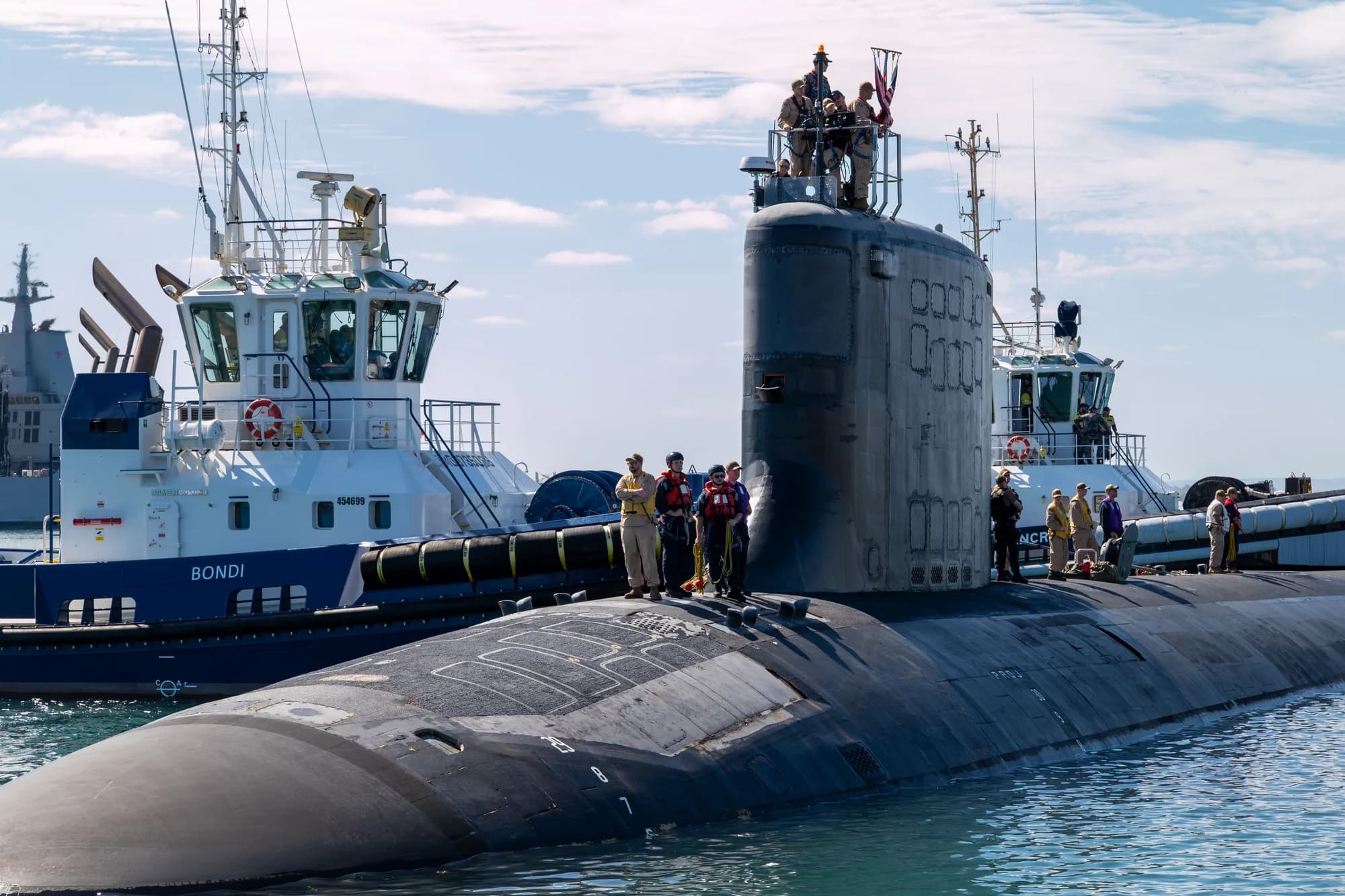 A United States Virginia-class fast-attack submarine alongside at HMAS Stirling, Western Australia, with commercial tugs on either side